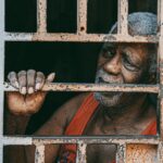 man in orange and blue shirt standing behind white metal window frame